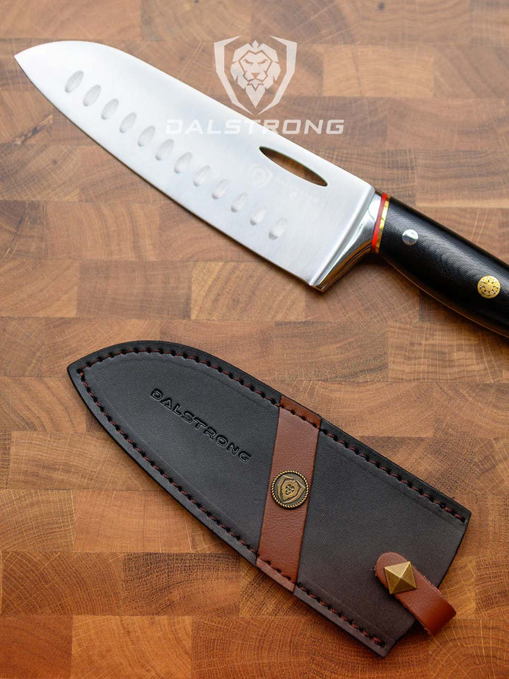 Dalstrong centurion series 7 inch santoku knife with black handle beside it's sheath.