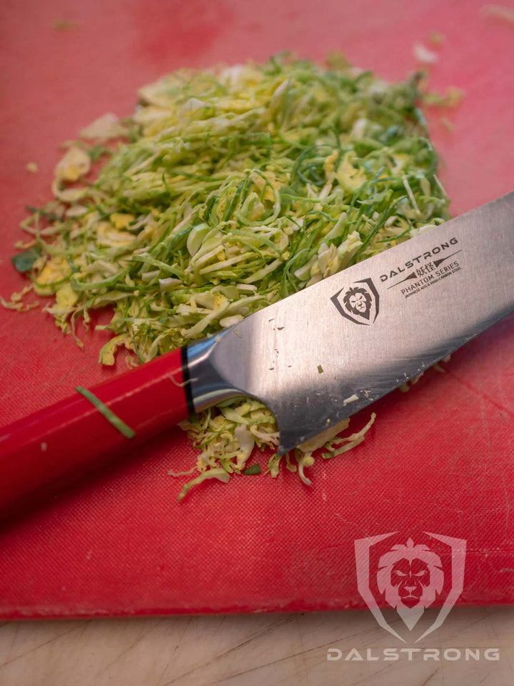Dalstrong phantom series 8 inch chef knife with red handle and chopped brussel sprouts on a red cutting board.