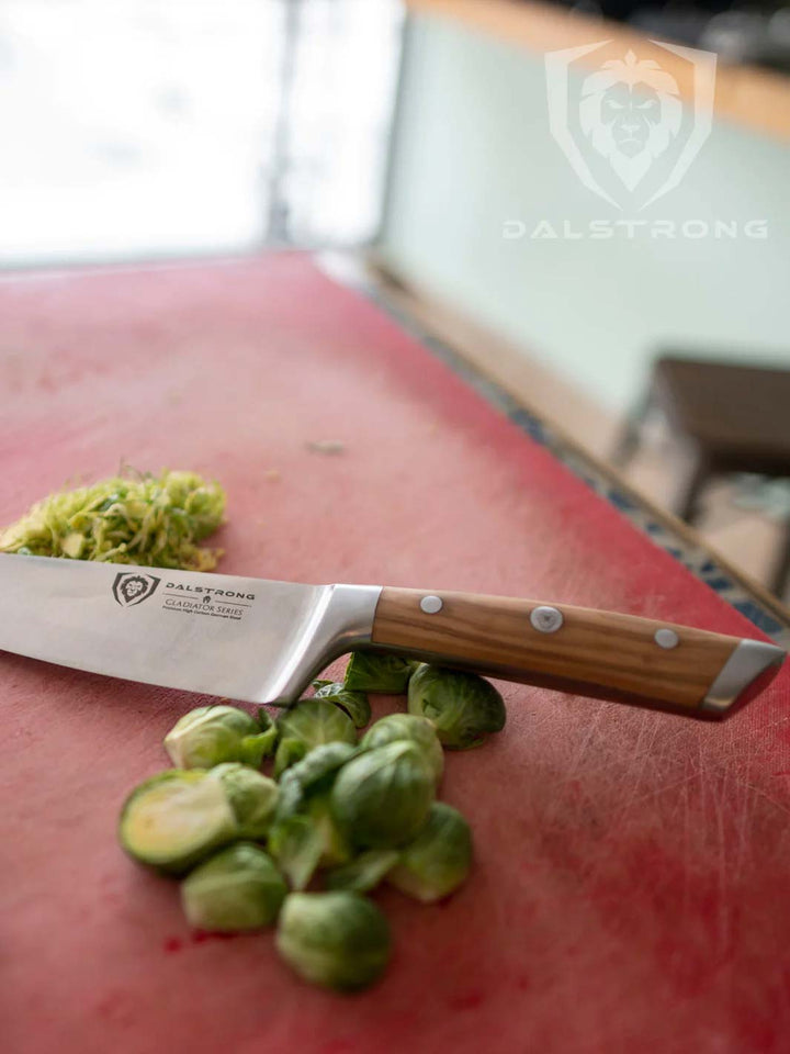 Dalstrong gladiator series 8 inch chef knife with olive wood handle and brussel sprouts beside it.
