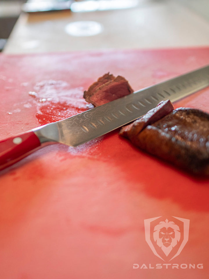 Dalstrong shogun series 12 inch slicer knife with crimson red handle and sliced steak on a red board.