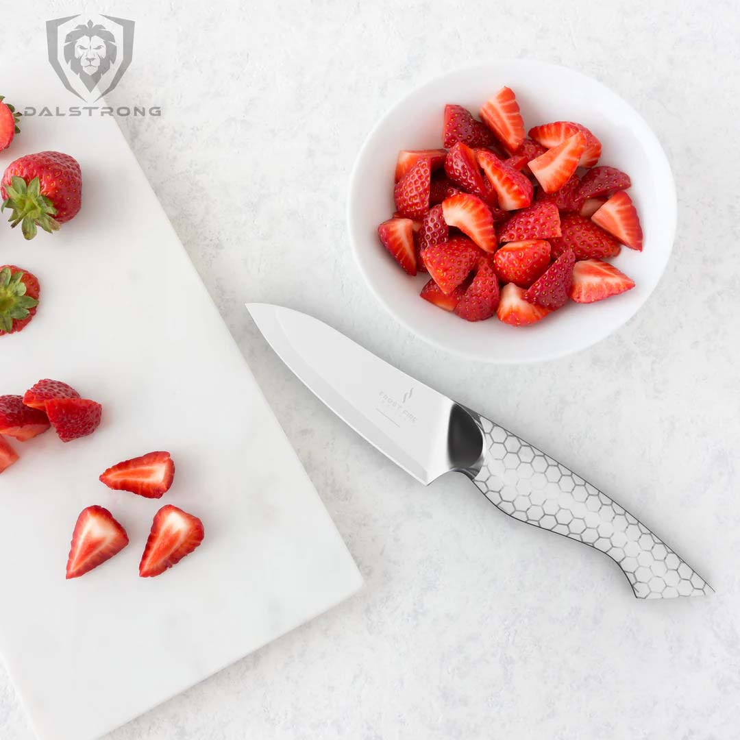Dalstrong frost fire series 3.5 inch paring knife with slices of strawberries on a white board.