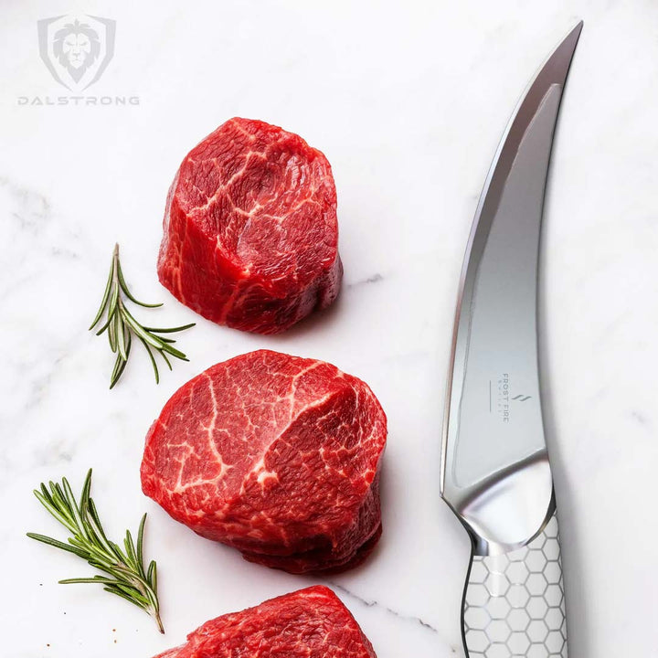 Dalstrong frost fire series 6 inch fillet knife with white handle beside three cuts of steak.