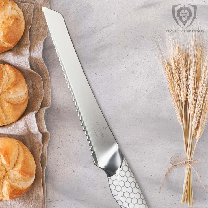 Dalstrong frost fire series 8 inch bread knife with white honeycomb handle and three bread on top of a cloth.