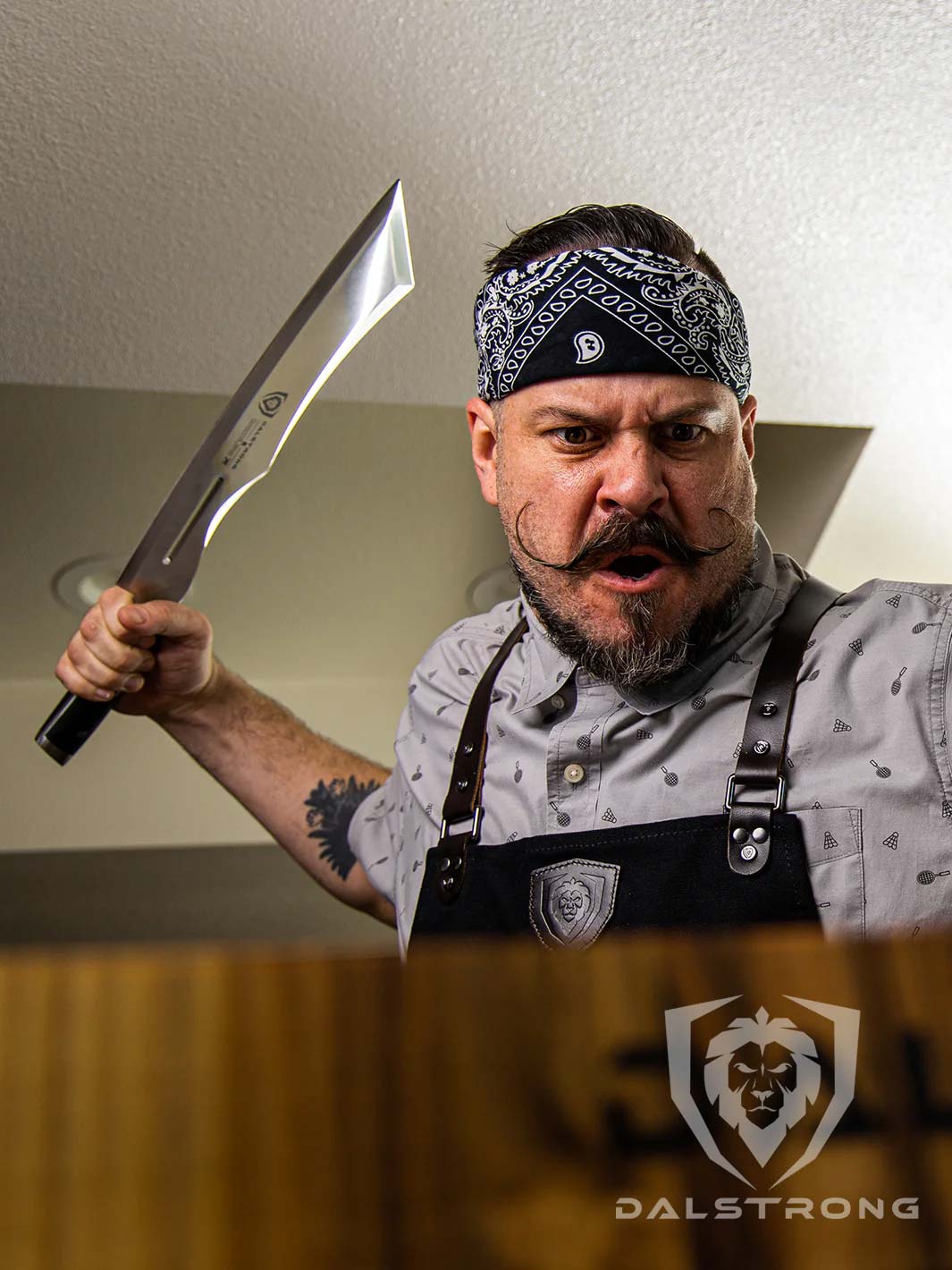 Man wearing a dalstrong kitchen apron and holding the dalstrong gladiator series 14 inch annihilator cleaver knife.