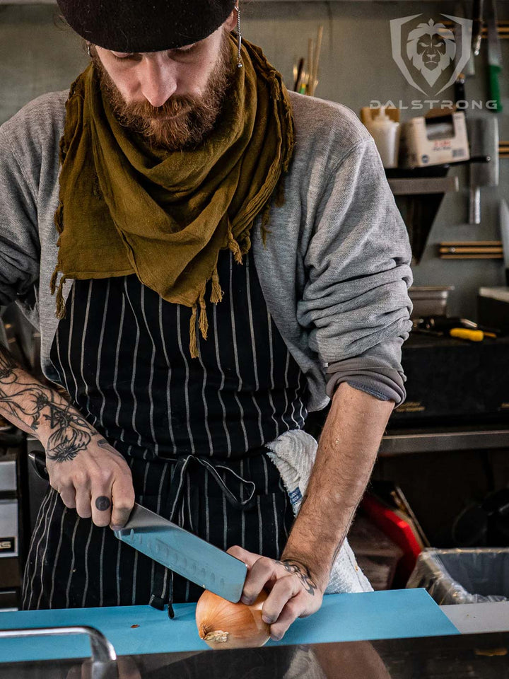 A man wearing a stripe apron holding the dalstrong gladiator series 7 inch nakiri knife with black handle.