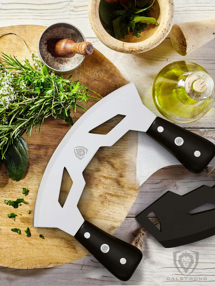 Dalstrong gladiator series 8.5 inch mezzaluna knife with black handle and green herbs on a cutting board.