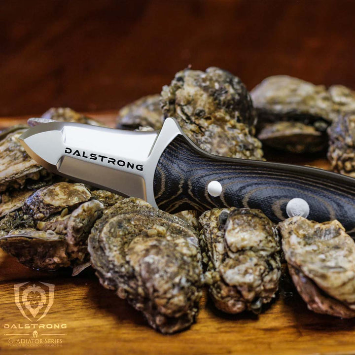 Dalstrong gladiator series 3 inch oyster knife with black handle on top of oysters on a wooden table.