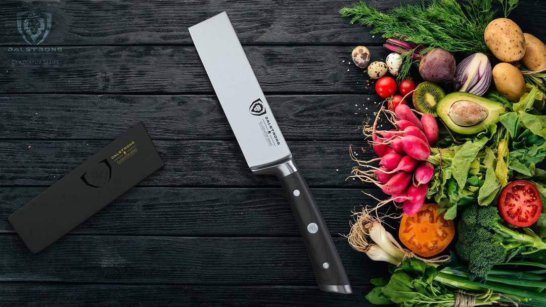 Dalstrong gladiator series 6 inch produce knife with black handle and sheath beside of different kinds of vegetables.