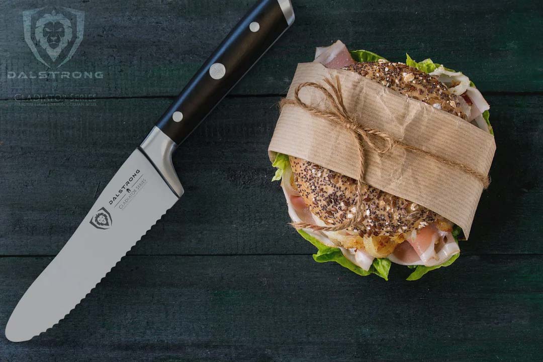 Dalstrong gladiator series 6 inch serrated sandwich knife with black handle and a sandwich on top of a wooden table.