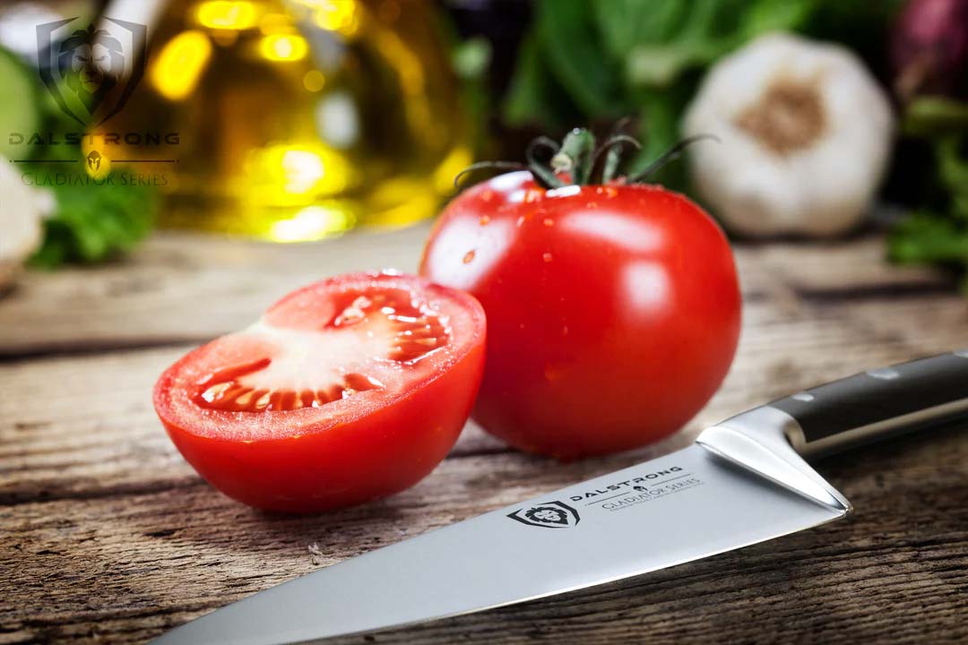 Dalstrong gladiator series 6 inch chef knife with black handle and two tomatoes on a wooden table.