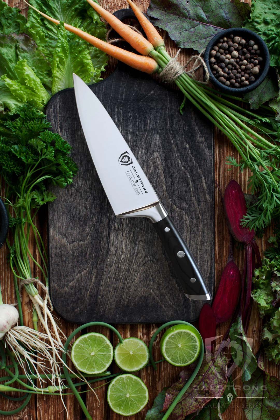 Dalstrong gladiator series 6 inch chef knife with black handle in the middle of vegetables and herbs.