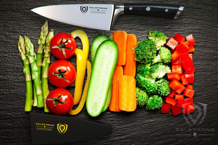 Dalstrong gladiator series 6 inch chef knife with black handle and sheath in between of different kinds of vegetables.