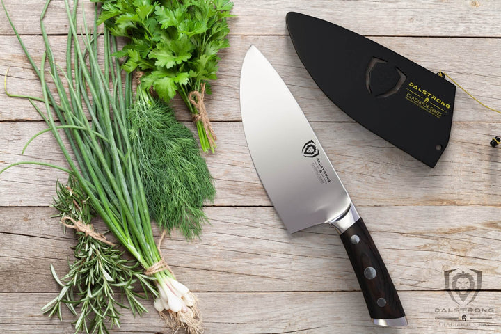 Dalstrong gladiator series 7 inch rocking herb knife with black handle and sheath beside some different herbs.