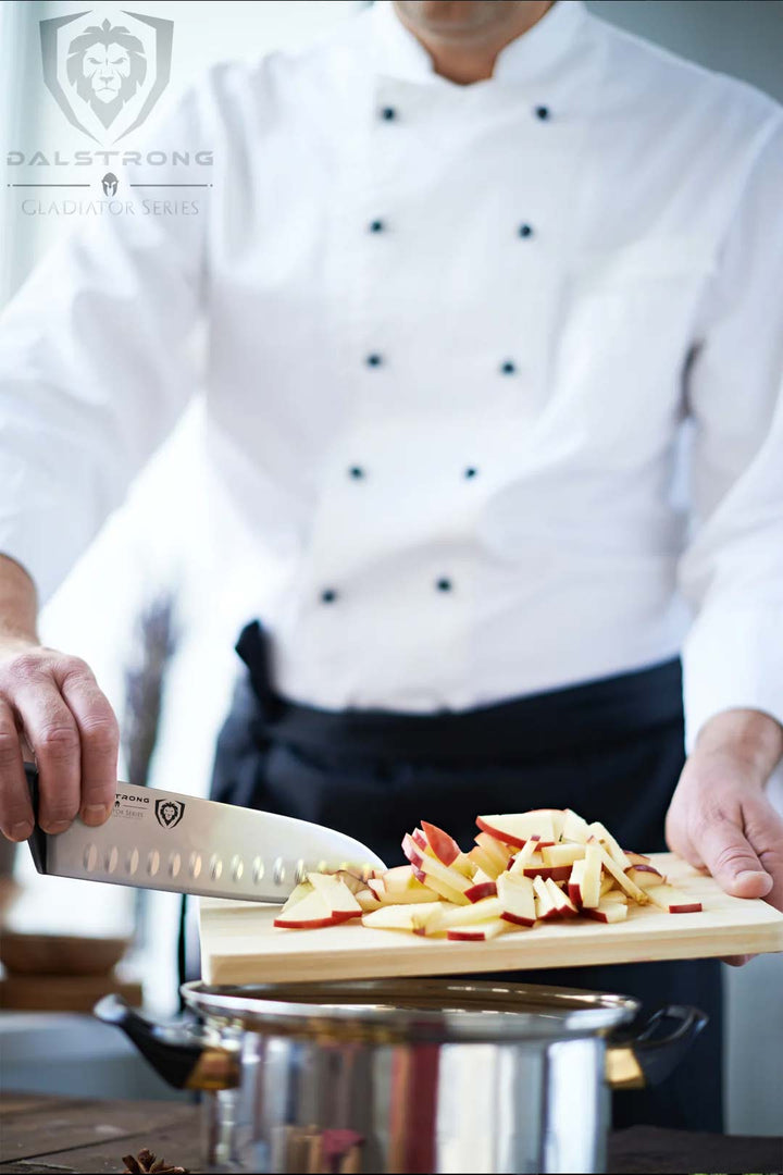 A chef holding the dalstrong gladiator series 7 inch santoku knife with chopped apples on a wooden board.