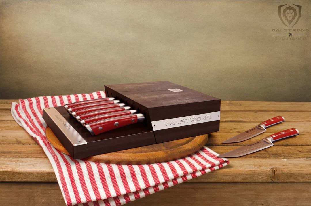 Dalstrong gladiator series 8 piece steak knife set with red handles inside of it's wooden block on top of a wooden cutting board.