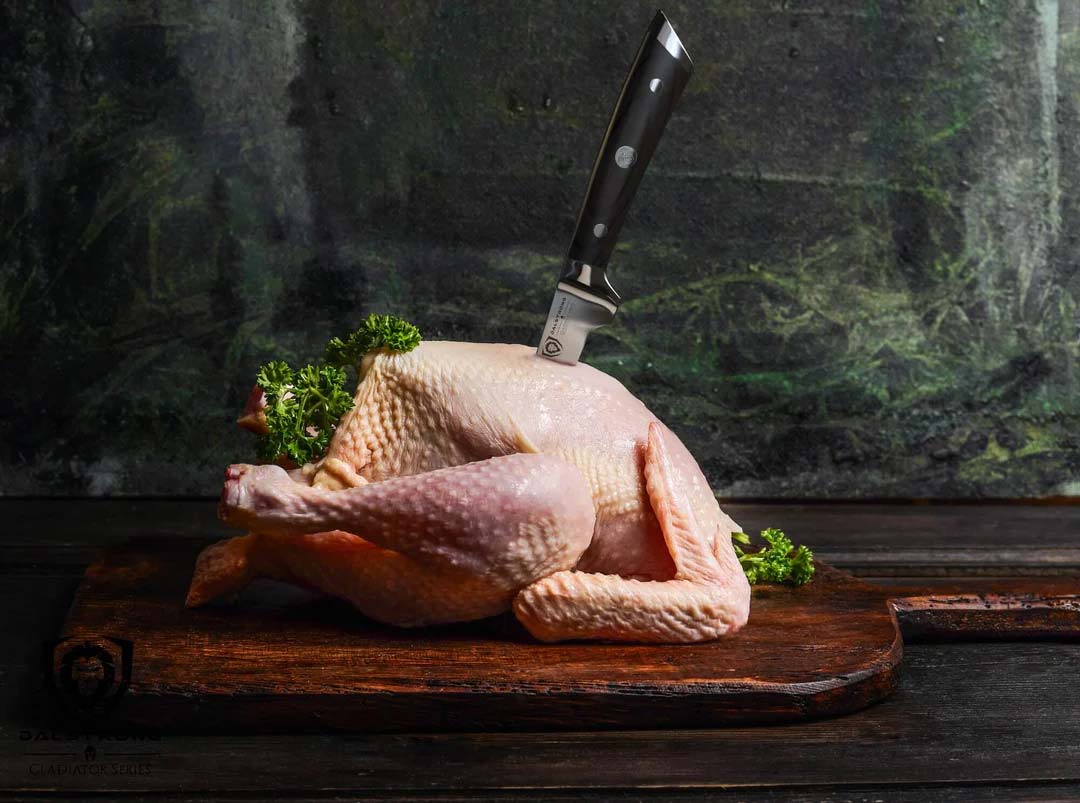 Dalstrong gladiator series 3.75 inch boning knife with black handle and a whole chicken on wooden board.
