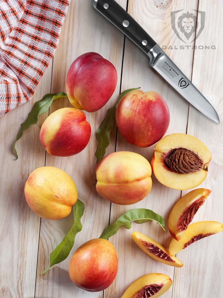 Dalstrong gladiator series 3.5 inch paring knife with black handle and peaches on top of a wooden table.