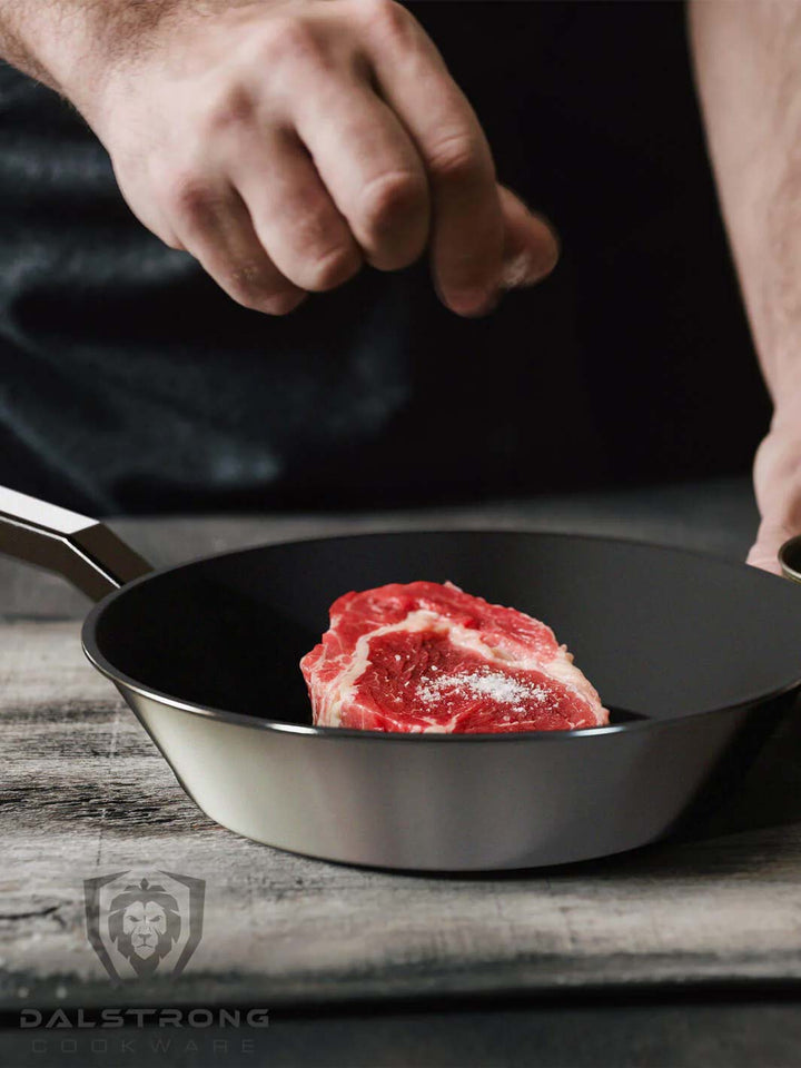 A man putting salt on a steak inside the Dalstrong oberon series 10 inch eterna non-stick frying pan and skillet.