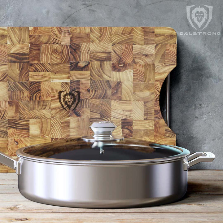 Dalstrong oberon series 9 inch eterna non-stick saute frying pan with lid beside a dalstrong cutting board.