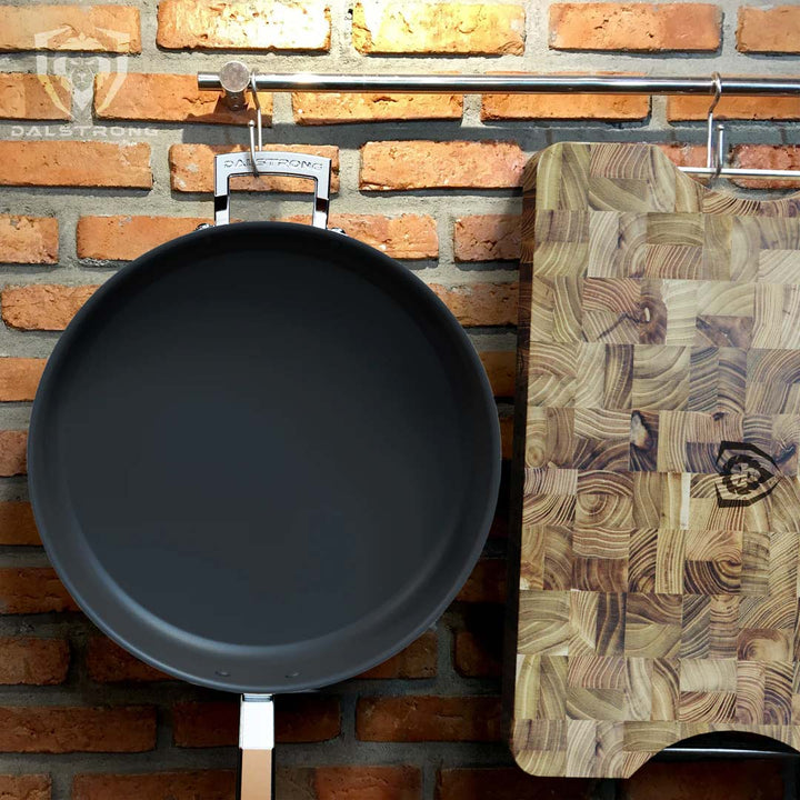 Dalstrong oberon series 9 inch eterna non-stick saute frying pan with lid hangin on a wall beside a dalstrong cutting board.