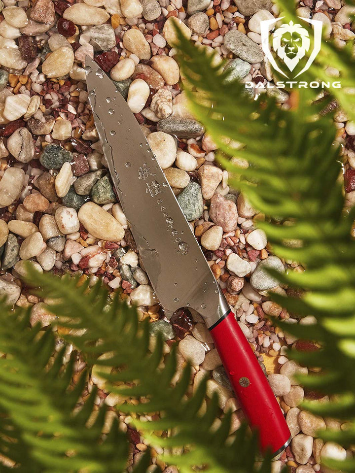 Dalstrong phantom series 8 inch chef knife with red handle on top of wet pebbles.