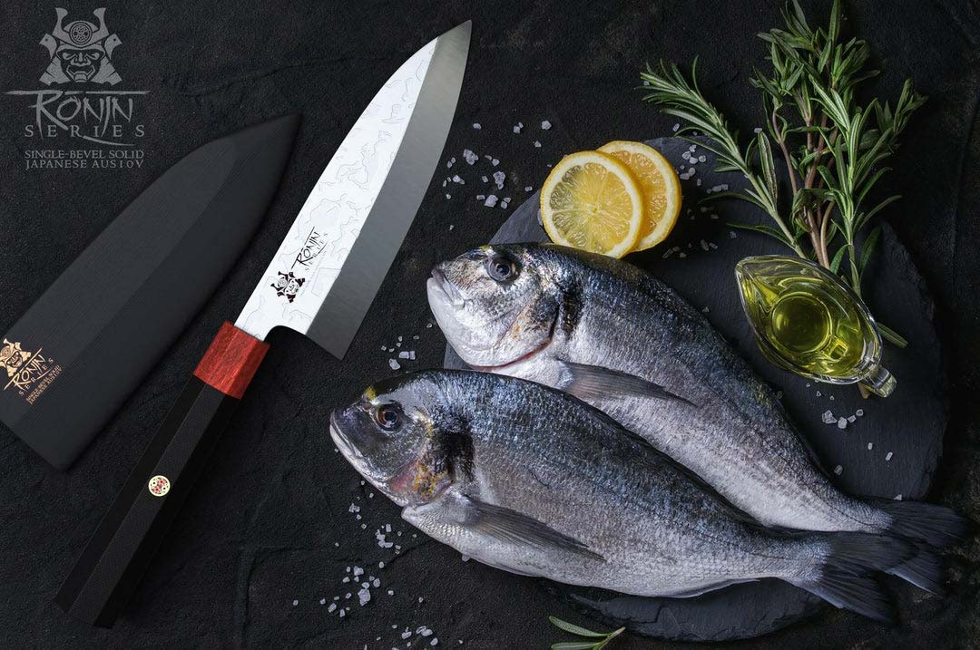 Dalstrong ronin series 6 inch deba knife with black handle and two whole fish on a cutting board.