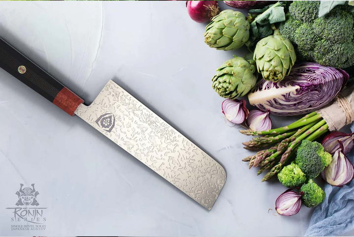 Dalstrong ronin series 7 inch usuba knife with black handle and sheath beside some vegetables.