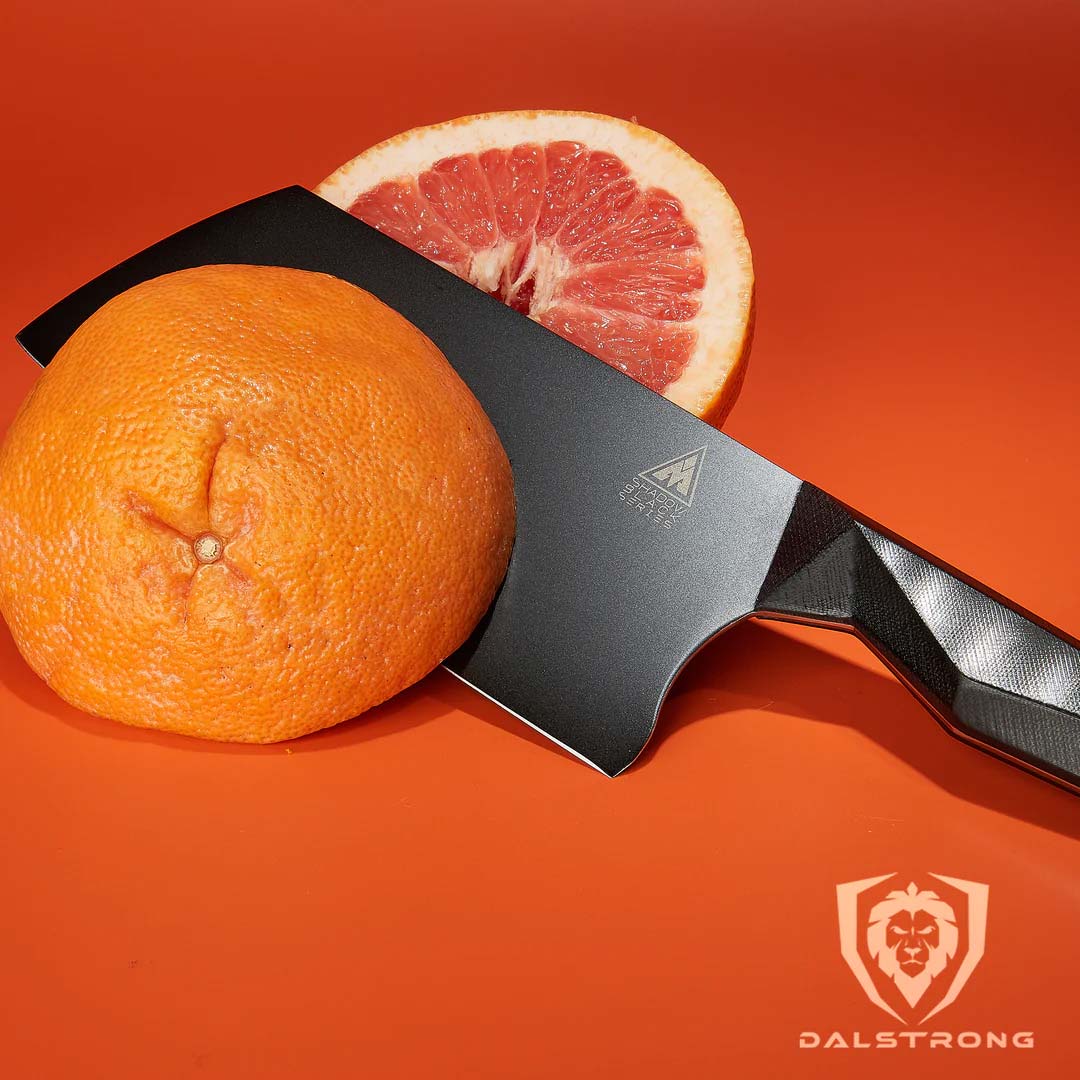 Dalstrong shadow black series 7 inch cleaver knife with two thin slices of orange.