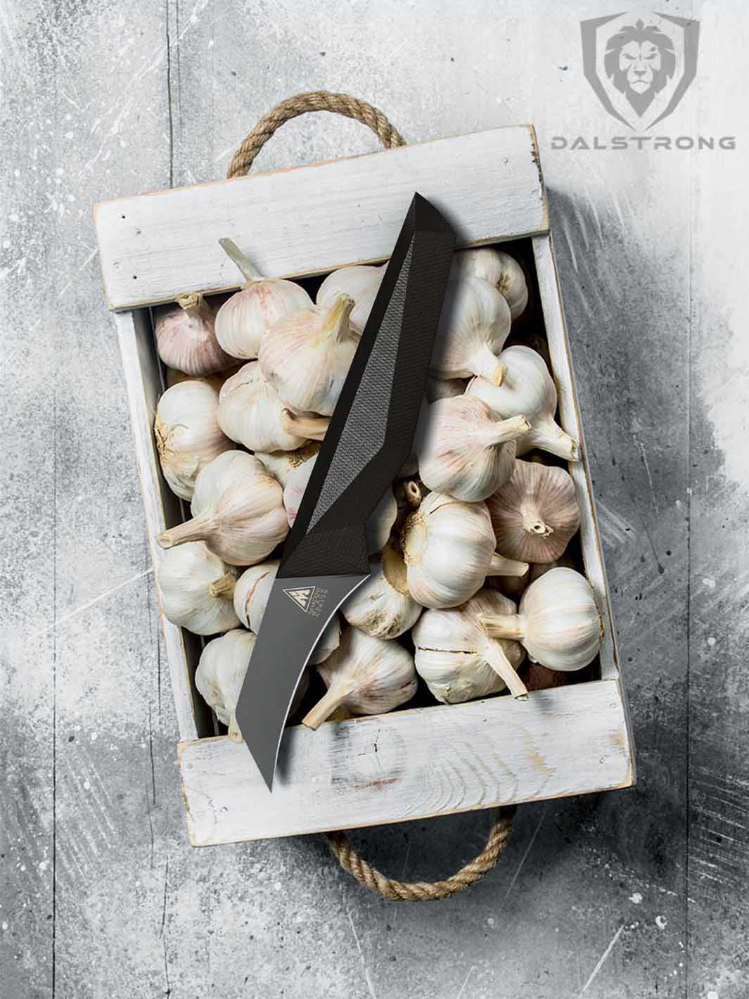 Dalstrong shadow black series 2.75 inch bird's beak paring knife with garlic cloves insise a wooden box.
