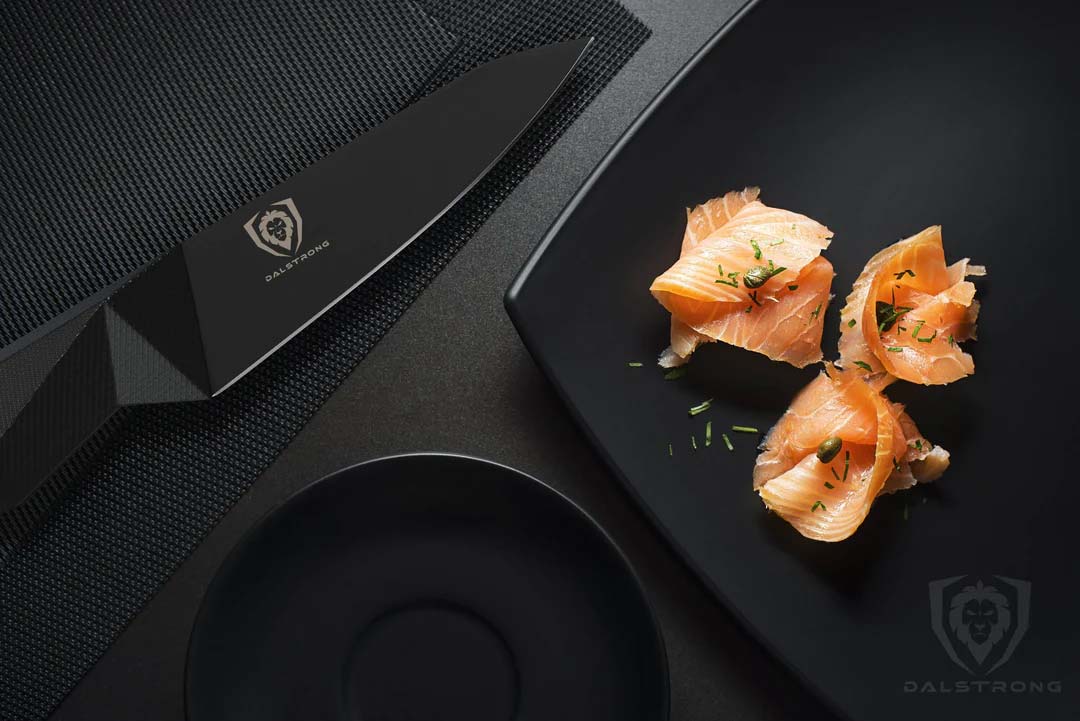 Dalstrong shadow black series 4 inch paring knife with thin slices of salmon on a black plate.