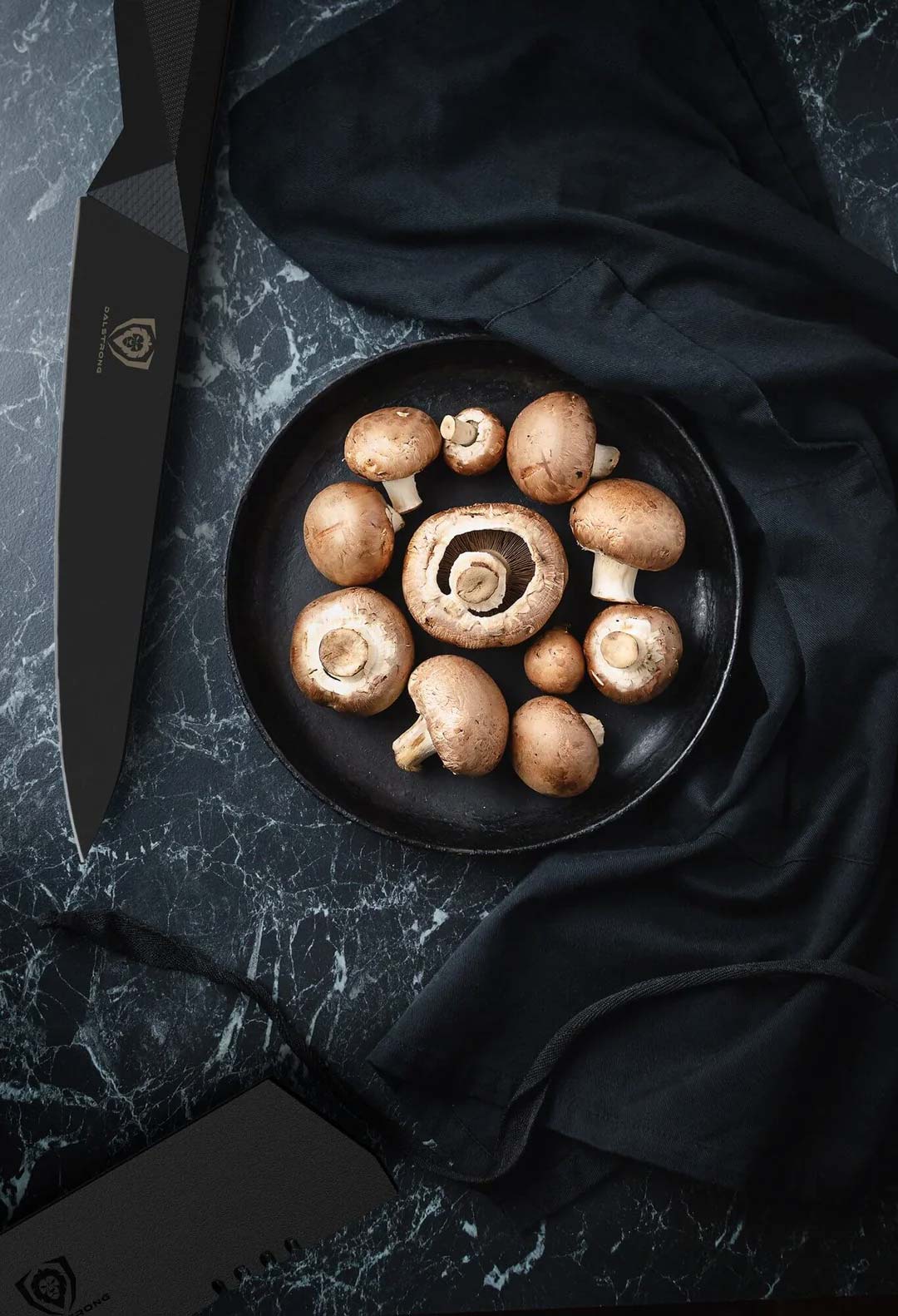 Dalstrong shadow black series 5.5 inch utility knife with black sheath beside some mushrooms.