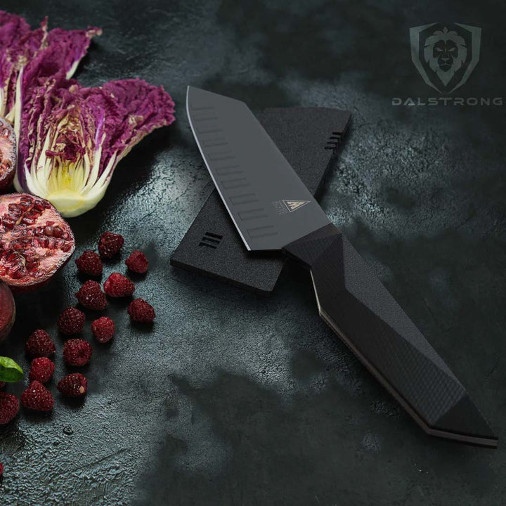 Dalstrong shadow black series 7 inch santoku knife with black sheath beside some fruits and vegetable.