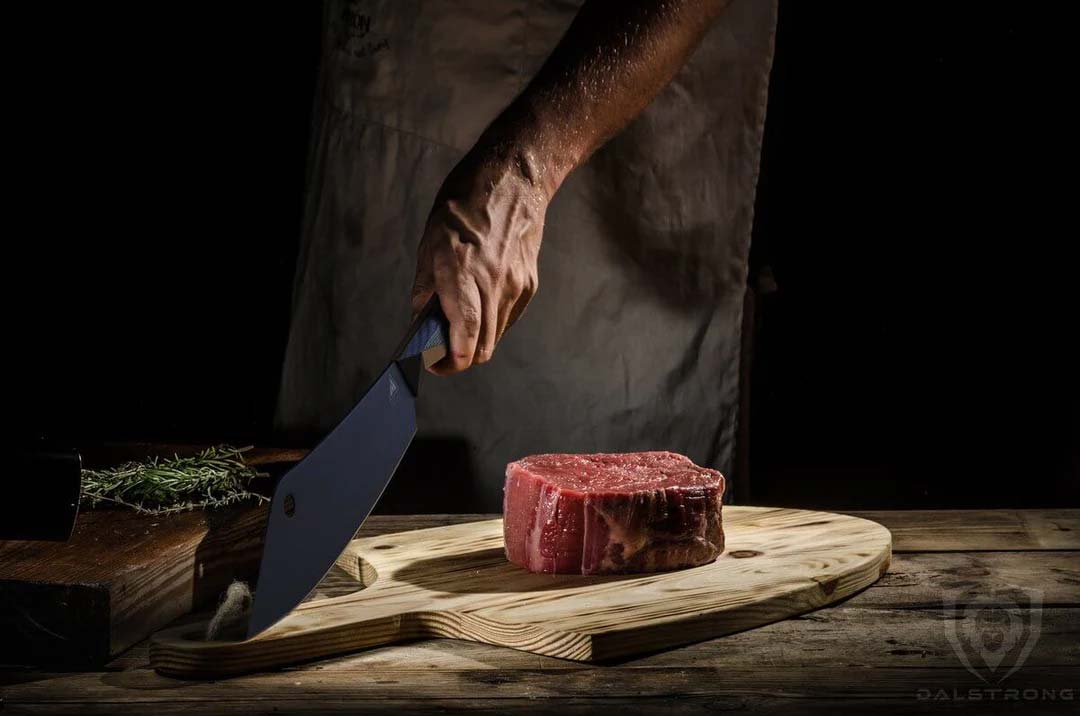 Dalstrong shadow black series 8 inch crixus cleaver knife with a thick cut of steak on a wooden cutting board.
