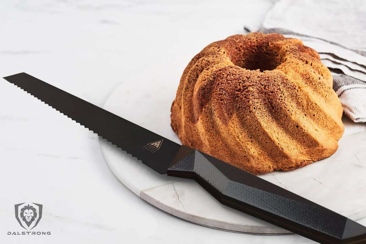 Dalstrong shadow black series 9 inch bread knife with a whole cake on a cutting board.