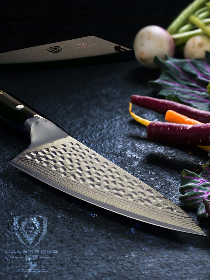 Dalstrong shogun series 6 inch chef knife with black handle with different kinds of vegetables beside.