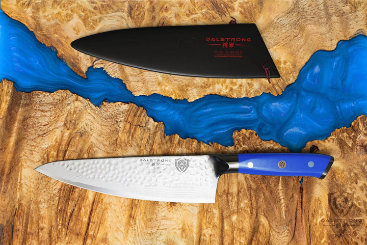 Dalstrong shogun series 8 inch chef knife with blue handle and black sheath on a wooden table with blue paint.