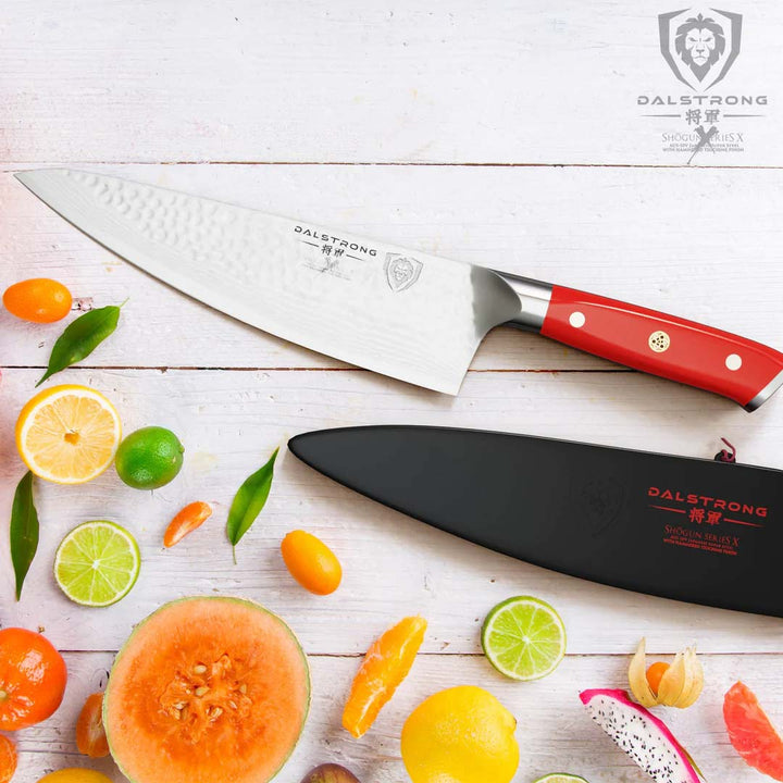 Dalstrong shogun series 8 inch chef knife with crimson red handle and sheath on top of different slices of fruits.