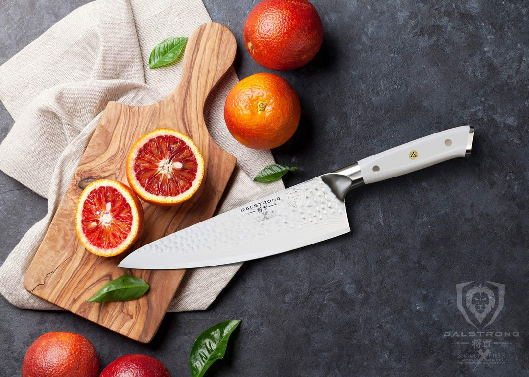 Dalstrong shogun series 8 inch chef knife with white handle and sliced orange in half on a wooden board.