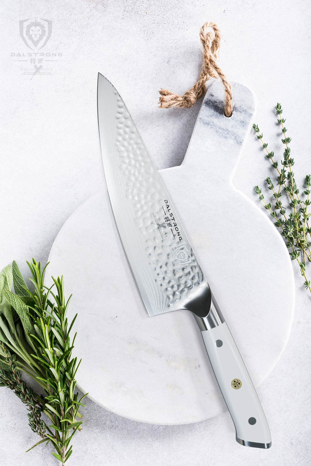 Dalstrong shogun series 8 inch chef knife with white handle on a white wooden board with green herbs beside it.