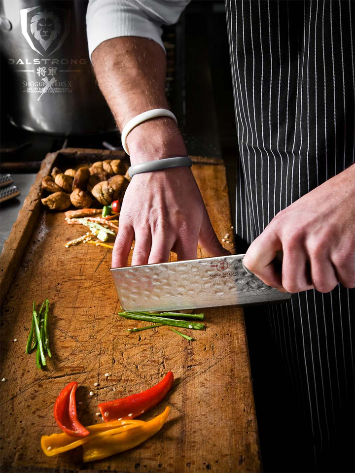 Dalstrong shogun series 6 inch nakiri knife with slices of bell peppers on top of a wooden board.
