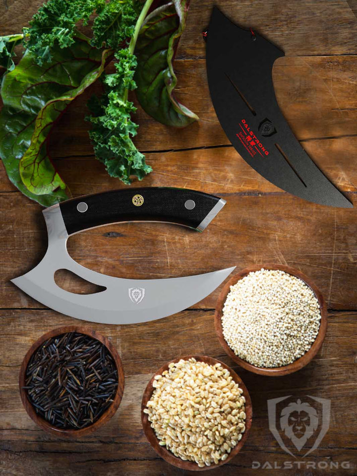 Dalstrong shogun series 6 inch ulu knife with black handle and sheath on a wooden table.