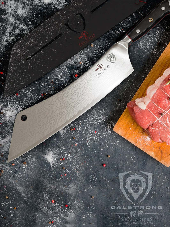 Dalstrong shogun series 12 inch crixus cleaver knife with black handle and sheath beside a large meat on a wooden board.