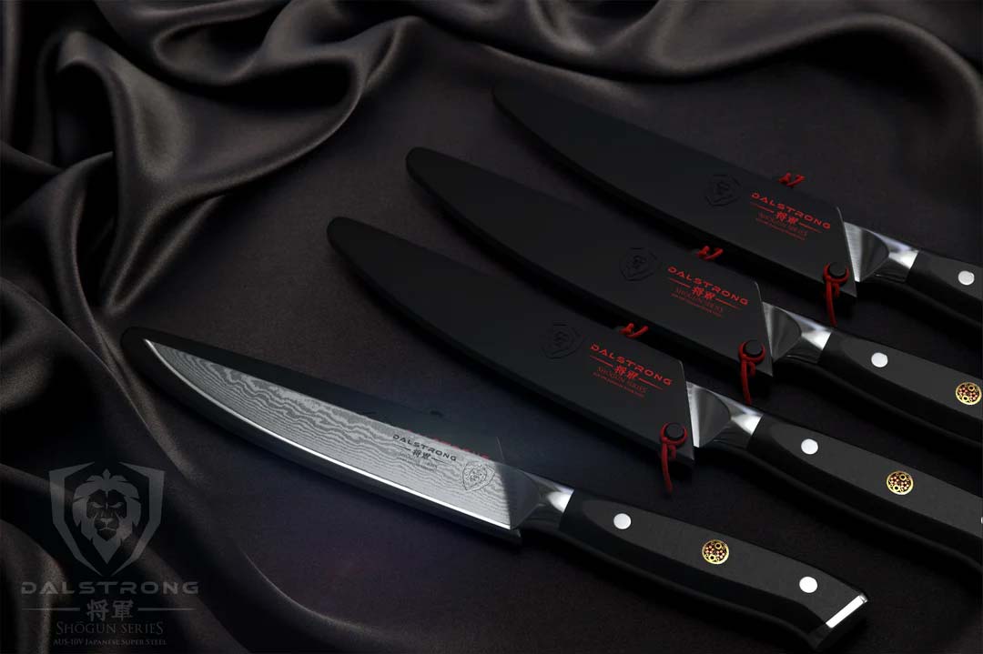Dalstrong shogun series 4 piece steak knife with black handle and sheath on a black cloth.