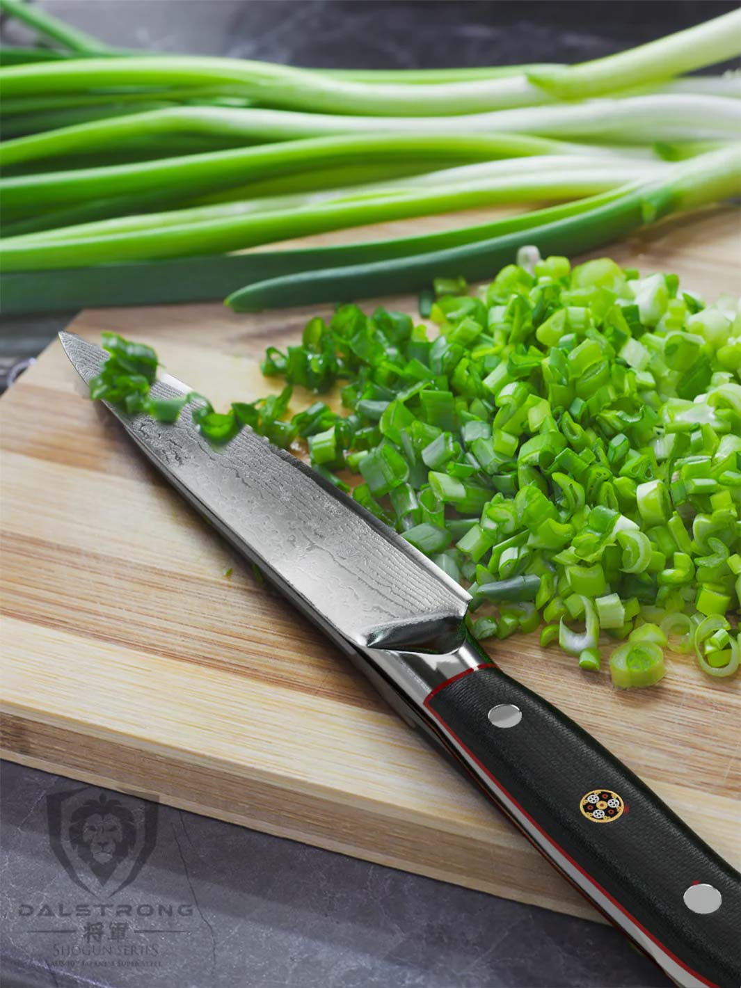 Dalstrong shogun series 6 inch utility knife with black handle and fresh scallions on a wooden board.