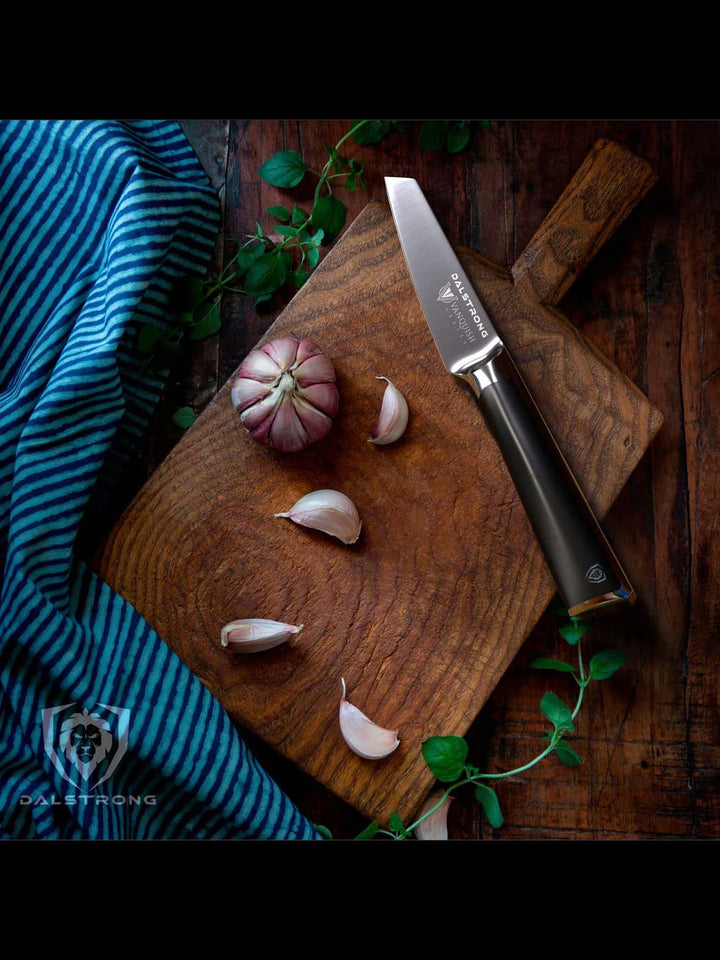 Dalstrong vanquish series 3.5 inch paring knife with black handle and garlic on a cutting board.