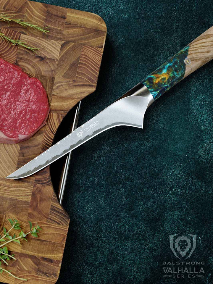 Dalstrong valhalla series boning knife with wooden handle and sheath beside a steak on a cutting board.
