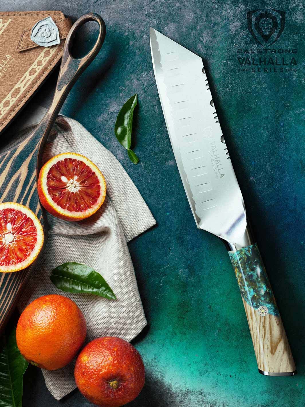 Dalstrong valhalla series 7 inch santoku knife with wooden handle and sheath beside slices of orange.