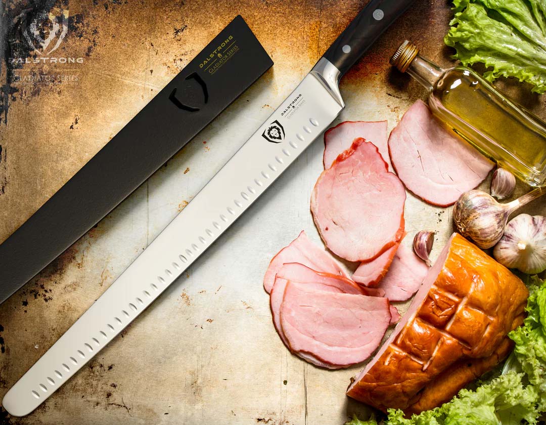 Dalstrong gladiator series 14 inch long slicer knif with black handle and sheath beside slices of ham.