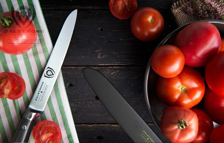 Dalstrong gladiator series 6 inch utility knife with black handle and sheath in between of red tomatoes.