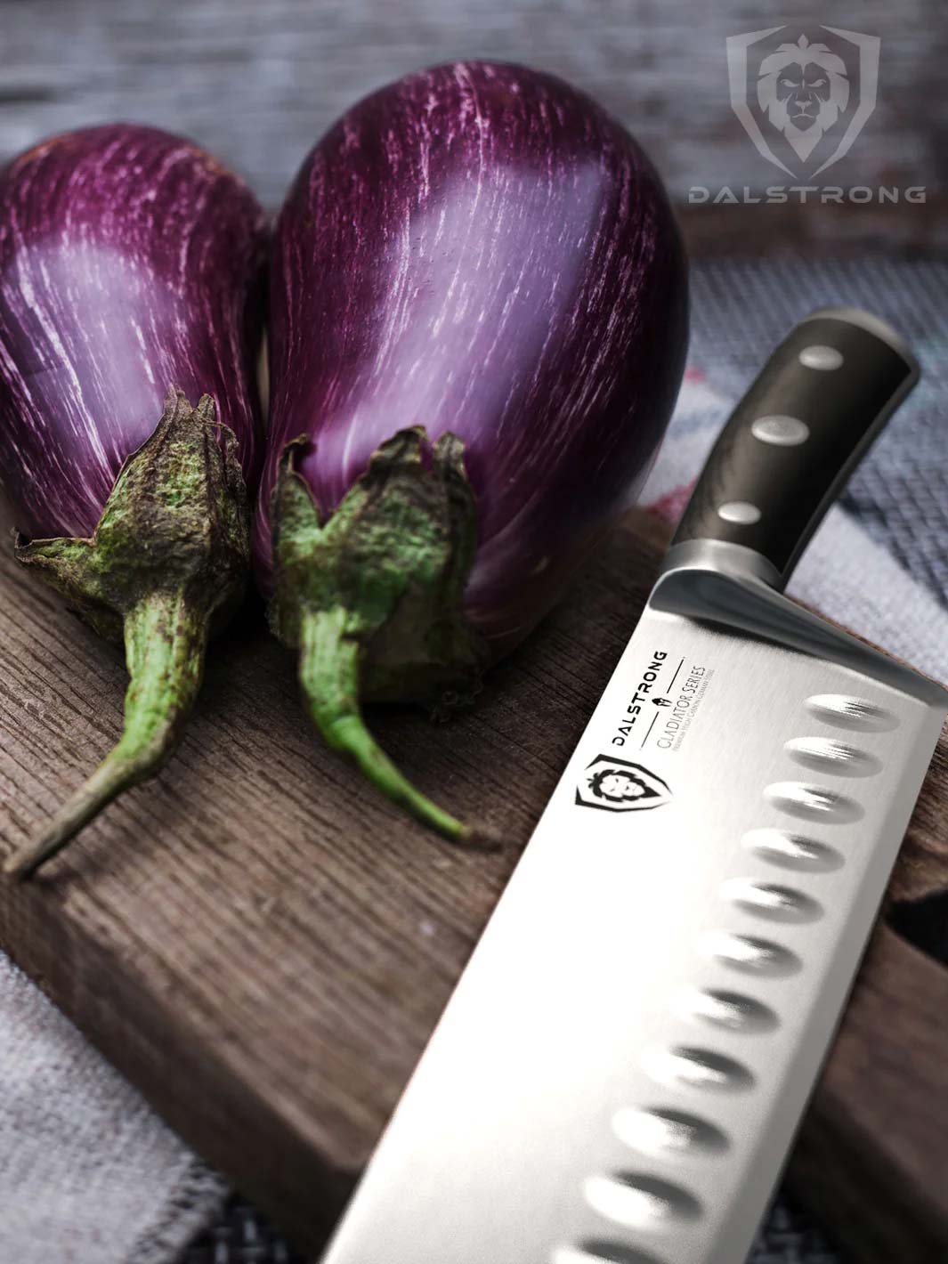 Dalstrong gladiator series 7 inch nakiri knife with black handle and two eggplants on a wooden cutting board.